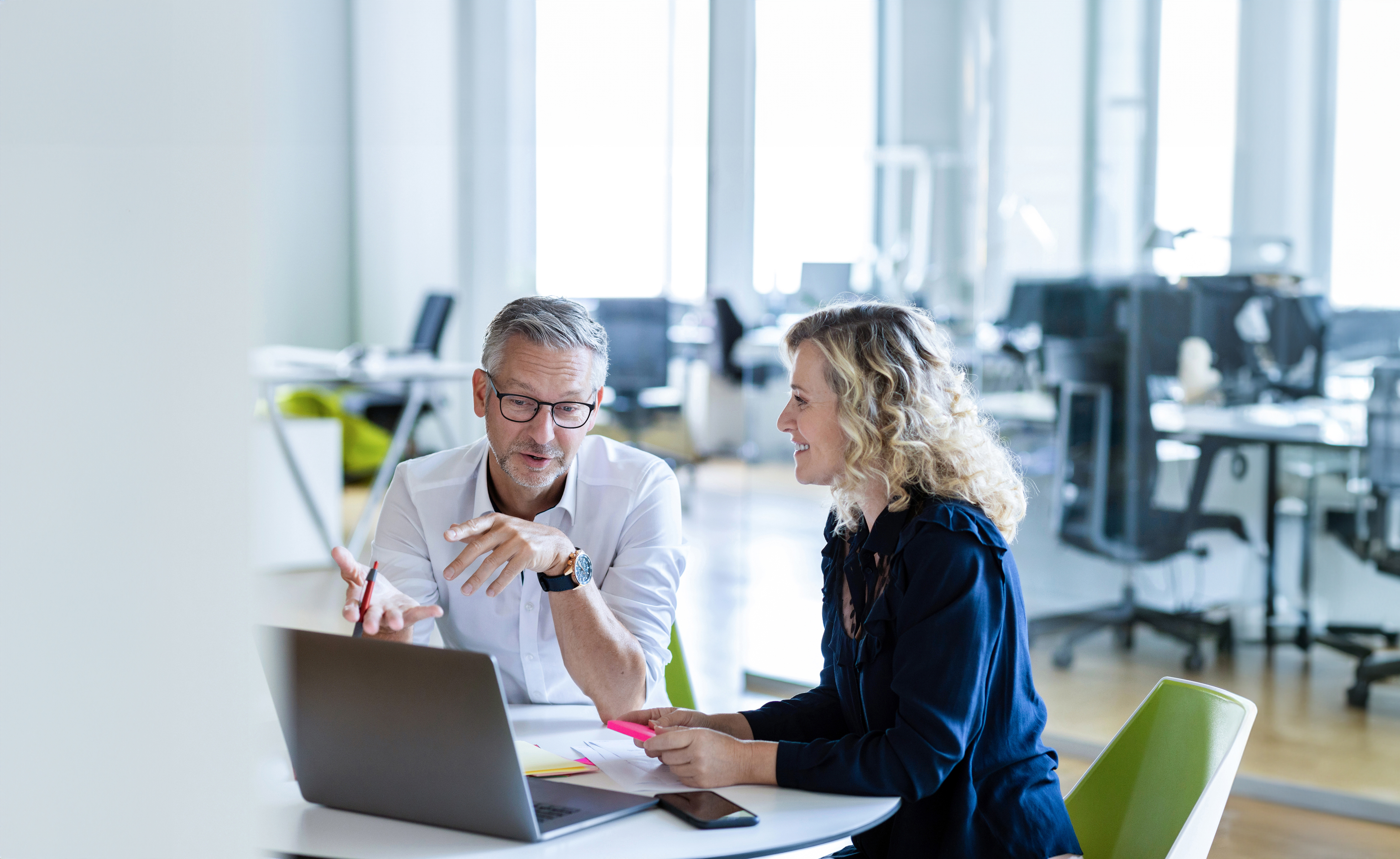 Ein Mann und eine Frau sitzen an einem Schreibtisch über einen Laptop gelehnt und unterhalten sich angeregt