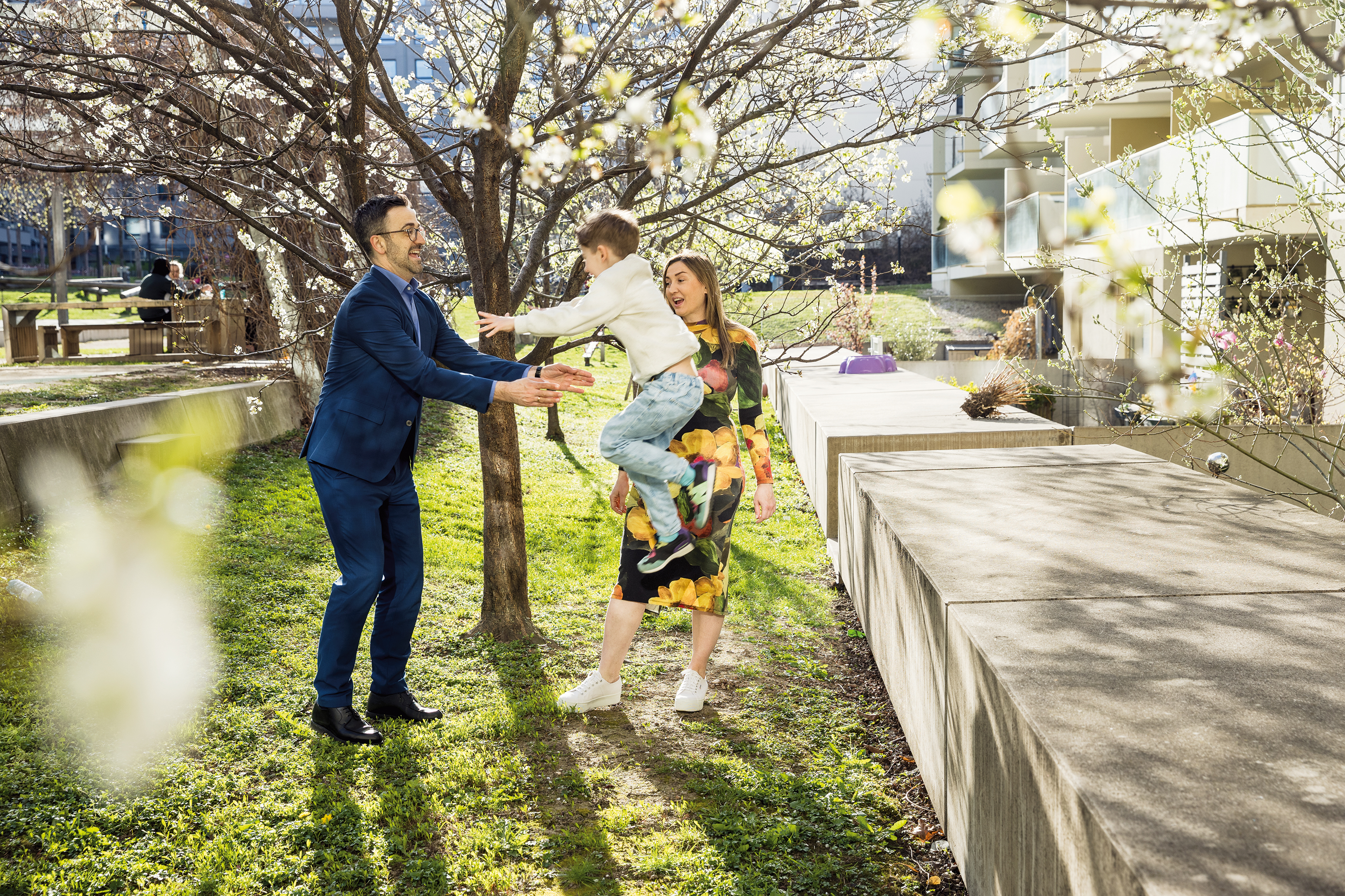 Ein Ehepaar spielt mit seinem jungen Sohn vor einer ÖSW Wohnbau bei Sonnenschein im Garten unter einem Baum