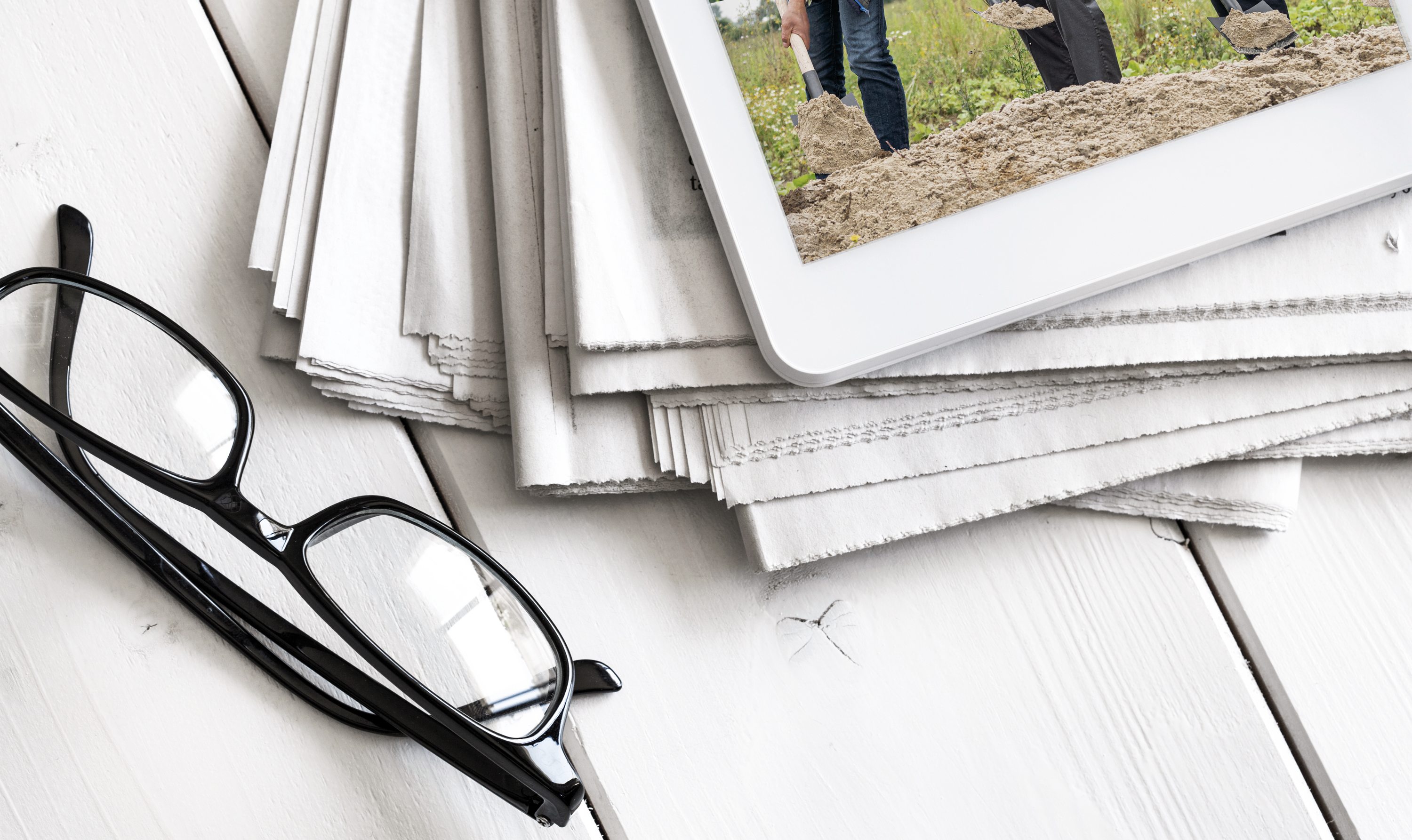 Neben einigen gestapelten Zeitungen liegt eine schwarze Brille auf einem weißen Tisch